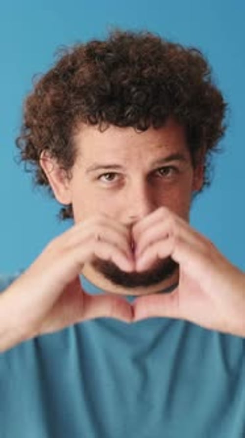 Close up, man showing representing heart gesture isolated on blue background in studio