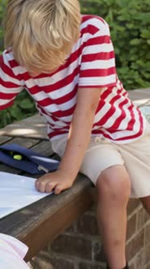 Vertical video: Placing page, boy holding pad and drawing work with pencil on bench in striped tee