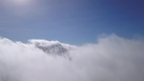 Shot from a drone flying over a group of clouds uncovering a bright blue sky and direct sunlight.
