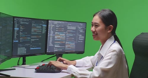 Asian Woman Developer Using Computer To Write Code With Multiple Screens In Green Screen Studio