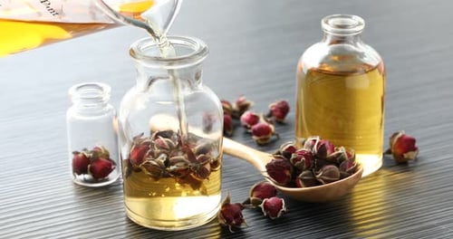 Pouring essential oil into open perfume bottles on grey wooden table, closeup