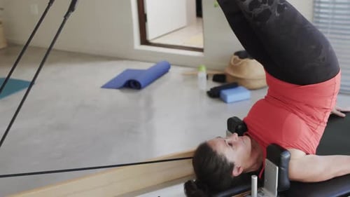 Fit senior caucasian woman stretching on reformer in pilates studio, unaltered, in slow motion