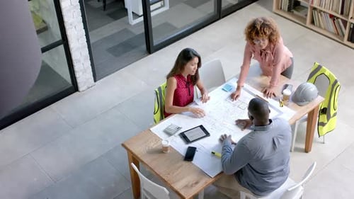 High angle of diverse architects discussing blueprints on table in office, copy space, slow motion