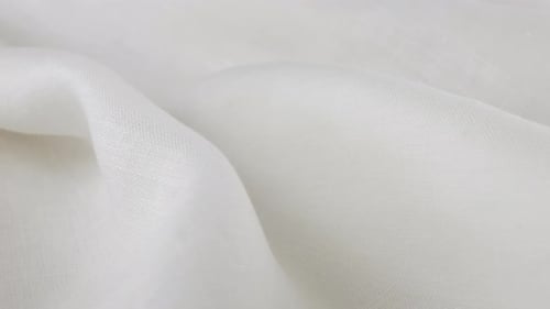 Weiche Falten des weißen Leinenstoffes drehen sich auf der Vitrine. Nahaufnahme des textilen Hintergrunds
.