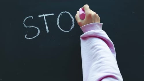 Closeup of a Timelapse of a Child's Hand Writing with Chalk on a Blackboard Stop Sexism