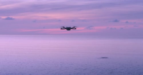 Modern Quadcopter Hovered in the Air and Flying to Sea Drone Quadcopter on Sea Background at Pink