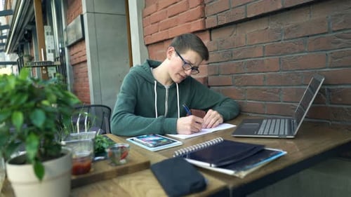 Young, Teenage Boy with Notepad Doing Homework by Table in Cafe Adolescent