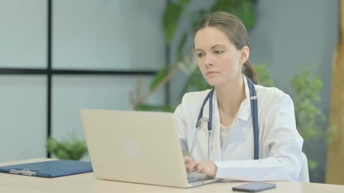 Busy Female Doctor Typing on Laptop in Clinic