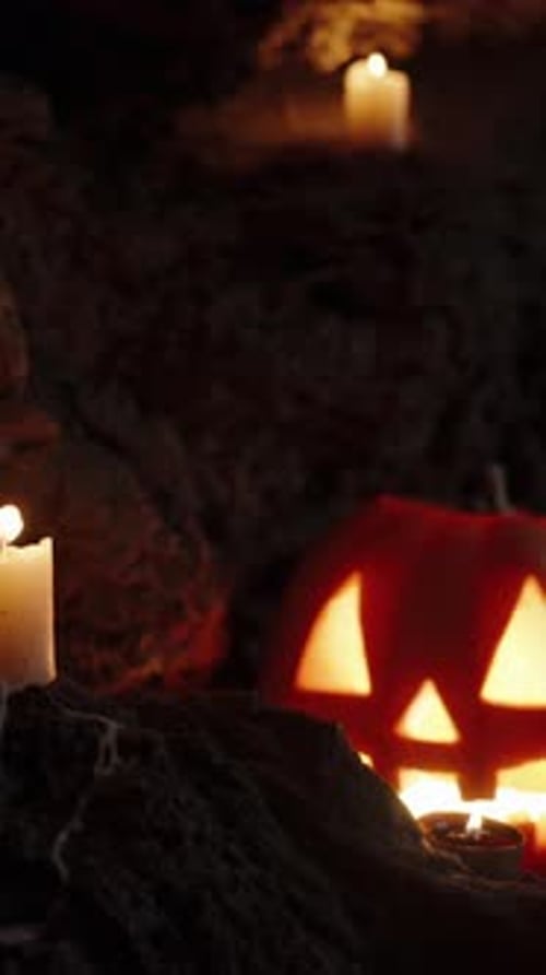 Vertical video. Jack-O'-Lantern Pumpkin in a Dark Cave, Wind Blowing Out Candles on the Rocks.