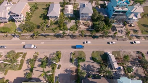 Birds eye drone footage starts over a road and then pull back and pans up to reveal beach houses.