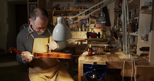 Master artisan carefully applying varnish on a new handcrafted violin in his workshop