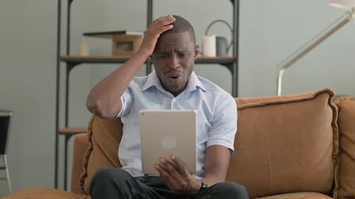 Man Sitting on Couch Reacts to Tablet