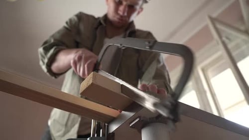 male craftsman works with wooden boards using a hand saw.