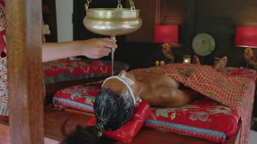 Oil flows steadily over the forehead of a woman receiving a relaxing Shirodhara treatment at an Ayur