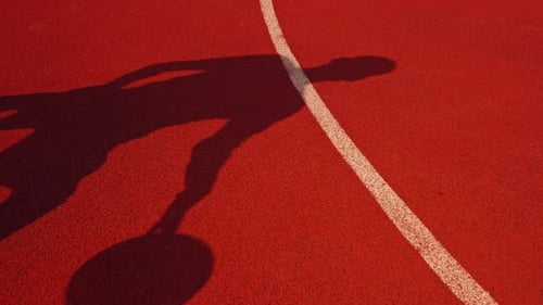 Close-up of a basketball guy's shadow on the floor of a basketball court while dribbling the ball