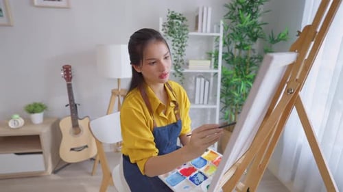 Asian young talented woman artist coloring on painting board in house.