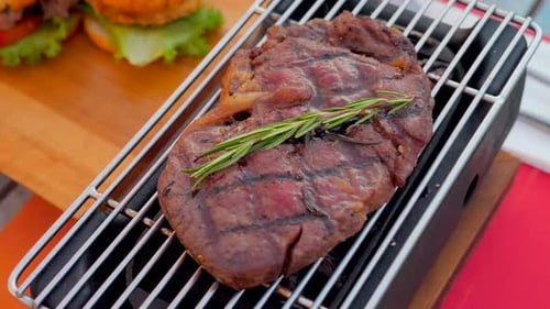 Juicy Beefsteak Cooks on Grill Grate with Rosemary