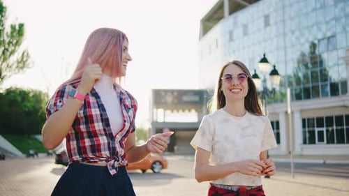 Two Beautiful Young Women are Walking in the Park at Sunset or Dawn and Talking to Each Other Two