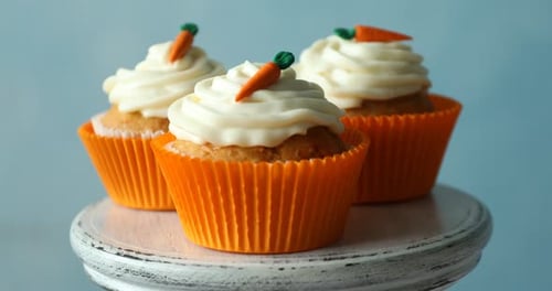 Delicious carrot cupcakes on stand against light blue background, closeup