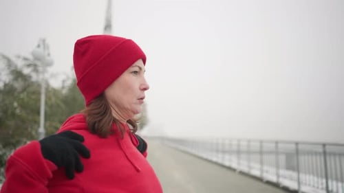 Athlete in Red Hoodie Performing Shoulder Stretch Outdoors in Snowy Winter Park