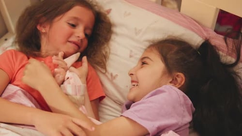 Two Girls Laughing and Holding Hands in Bed