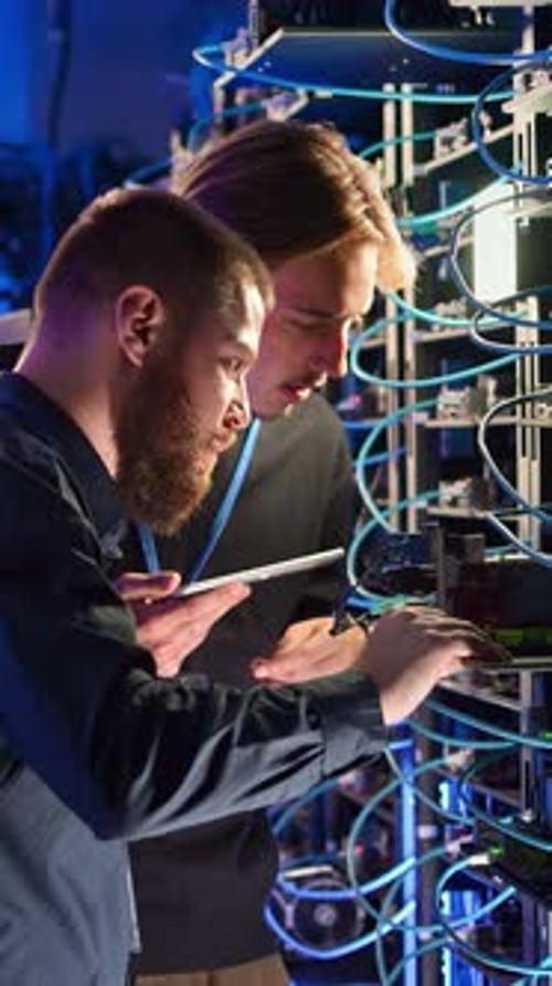 Two men analysing servers in a data centre. Vertical