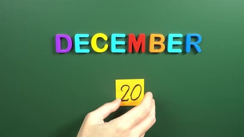 Hand sticking a sticker 20 December calendar day on school board. 20 date of December. Twentieth
