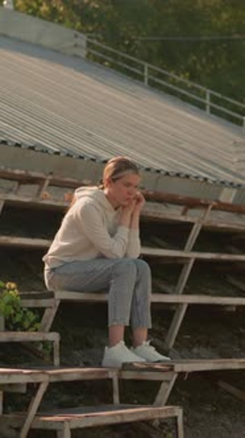 Thoughtful Woman in Casual Attire Sitting on Rustic Stadium Bleachers