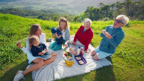 Big Family Have Picnic on the Green Hill in the Mountains at Sunrise