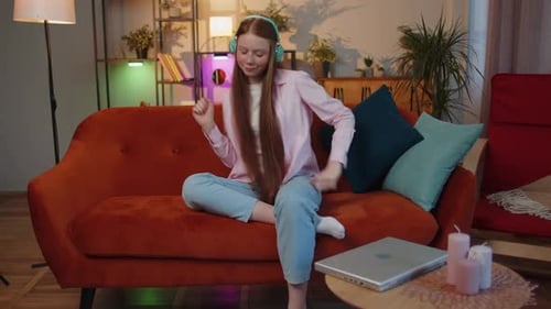 Happy Relaxed Kid in Wireless Headphones Dancing Listening Favorite Rock n Roll Music on Home Couch