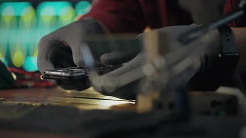 Hardware. Technician uses tools repairs phone in tech shop. Close-up Caucasian worker removes chip