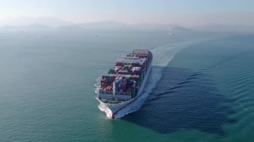 Aerial front view of a loaded container cargo vessel traveling over ocean.