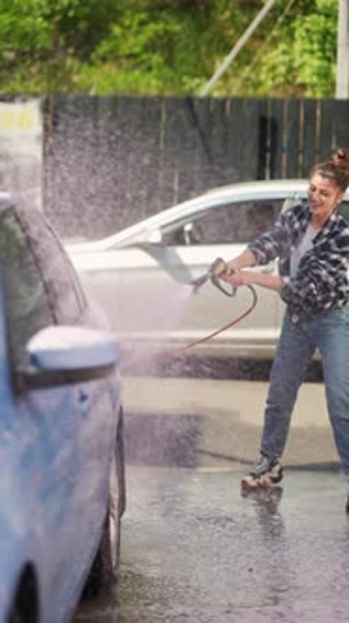 With a Foam Gun in Hand an Exuberant Girl Washes Her Car at the Car Wash