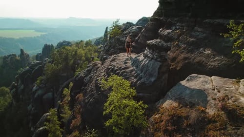 Woman walks alone on a rocky outcrop in Schrammsteine Elbe Sandstone Mountains with trees and rock f