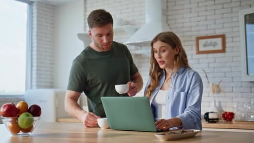 Couple Using Laptop with Coffee in Kitchen