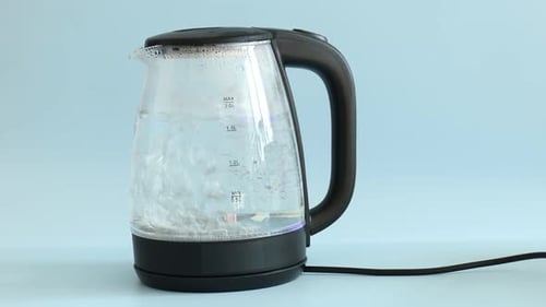 Water boiling in electric kettle on light blue background