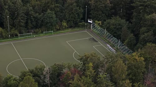 Aerial Flight besides an empty, green football field in the middle of the forest, Drone Footage