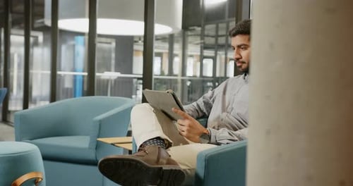 Thinking and holding tablet, businessman sitting in modern office lounge area