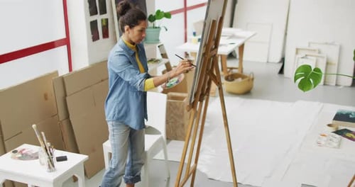 Video of biracial female artist painting in studio