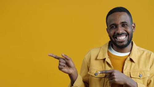 Portrait of Satisfied African American Man Pointing Sidewards and Laughing Looking at Camera