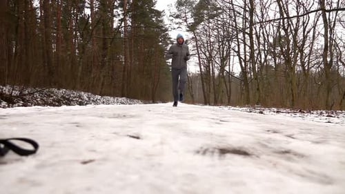 Young man jogging through a snowy winter forest in super slow motion