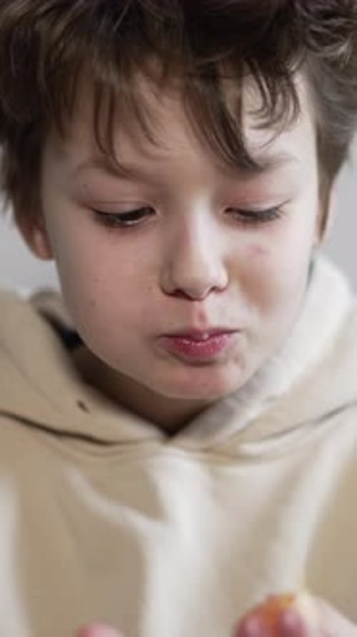 Cute boy with dark disheveled hair eats a juicy tangerine.