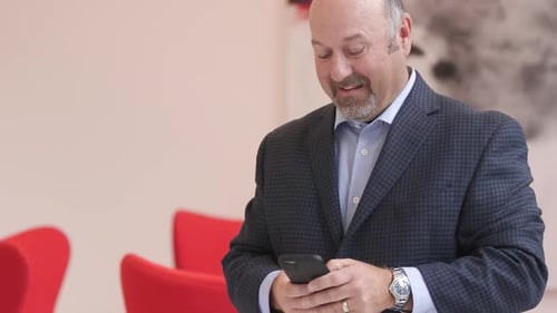 Man in Suit Smiling at Phone Inside Building