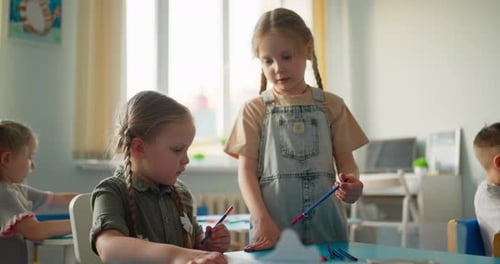 Kleine Kinder zeichnen zusammen an einem Klassentisch und teilen sich während einer kreativen Arbeit Buntstifte