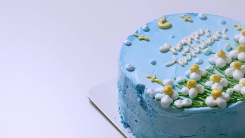 Close-up shot of the top of a birthday cake with blue frosting and decorated with white and yellow f