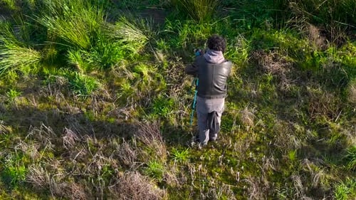 Above View Of A Photographer Keeping His Tripod And Camera In Grassy Nature Landscape. Aerial Shot