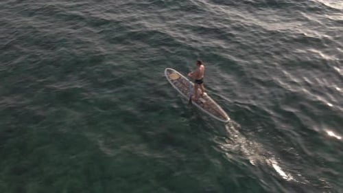 Aerial drone bird's eye view of Caucasian man exercising on a sup paddle board in turquoise tropical