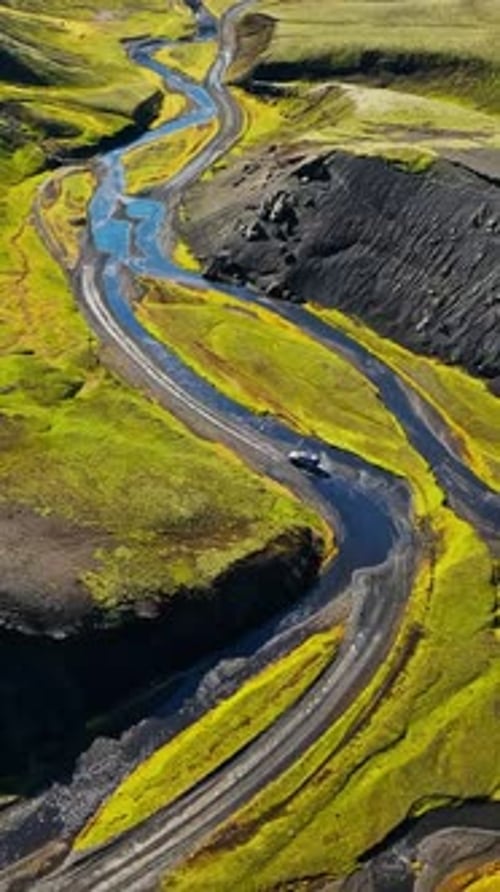 Vertical drone view of an S-shaped river beside a gravel road as a 4x4 crosses the Iceland