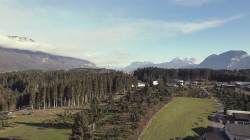 Drone aérien d'une magnifique chaîne de montagnes alpines au loin avec des champs gazonnés, des arbres et une ville