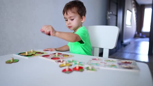 Focused baby boy playing with puzzles at desk. Cute kid learning fruit through a game.